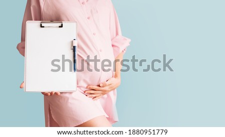 Pregnant woman with empty white paper as medical card, agreement blank. Concept of signing vaccination contract, work paper, writing birth plan. Healthcare checkup during pregnancy. Template for text. Royalty-Free Stock Photo #1880951779