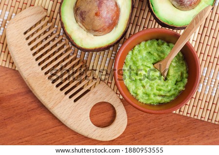 Fresh avocado puree in a small bowl and wooden hairbrush. Homemade face or hair mask, natural beauty treatment and spa recipe. Top view, copy space.  Royalty-Free Stock Photo #1880953555