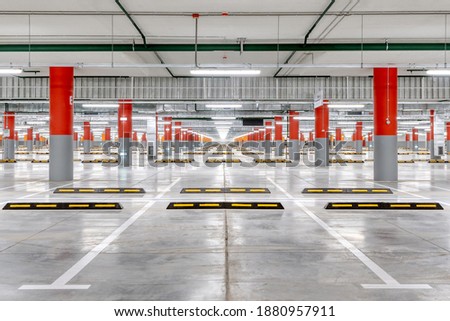 Large underground parking for cars. Empty new parking lot with bright lighting. The columns are painted red and orange.