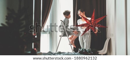 Mother and son decorating home and window for Christmas with red star Magic of winter holidays Family time