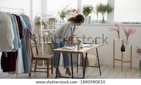 Daily routine. Concentrated young self employed woman dressmaker stand by desk at workspace focused on paperwork. Female decorator floral designer planning checking order information at cozy showroom Royalty-Free Stock Photo #1880980810