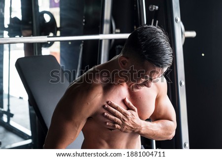 An asian male suffers a torn pectoral muscle while doing heavy incline bench presses on a Smith Machine at a gym or fitness center. A common workout injury Royalty-Free Stock Photo #1881004711