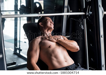 An asian male suffers a torn pectoral muscle while doing heavy incline bench presses on a Smith Machine at a gym or fitness center. A common workout injury Royalty-Free Stock Photo #1881004714