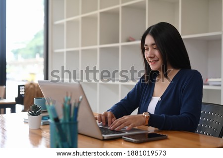 Young female designer working on freelance is browsing information for project on laptop at creative workstation.