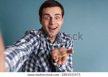 Happy young casual man taking a selfie while standing isolated over blue background