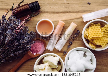 Ingredients for homemade lip balm: shea butter, essential oil, mineral color powder, beeswax, coconut oil. Homemade lip balm lipstick mixture with ingredients scattered around. Royalty-Free Stock Photo #1881045313
