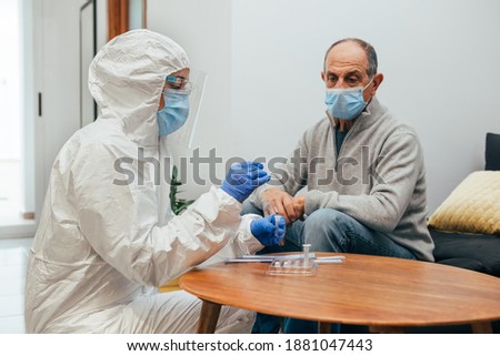 Health professional in a PPE suit, mask, face shield taking a nasal culture sample in the coronavirus pandemic during a home visit. Antigen test of an elderly patient.