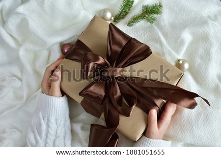 Female's hands in white pullover holding gift box with brown ribbon on white background. Christmas, New Year, Valentine's day and birthday concept.Copy spase. Selective focus