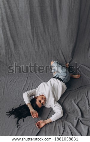Photoshoot of a young brunette. Girl in jeans. Grey background.