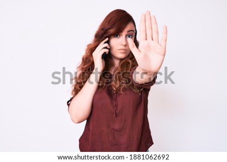 Young beautiful woman having conversation talking on the smartphone with open hand doing stop sign with serious and confident expression, defense gesture 