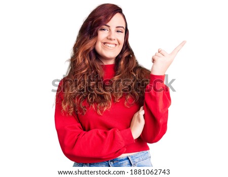 Young beautiful woman wearing casual winter sweater with a big smile on face, pointing with hand and finger to the side looking at the camera. 