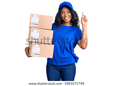 Young african american woman holding delivery package surprised with an idea or question pointing finger with happy face, number one 