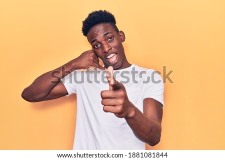 Young african american man wearing casual clothes smiling doing talking on the telephone gesture and pointing to you. call me. 