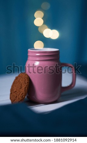 Pink cup of warm tea with ginger cookie on the blue background with blurred lights