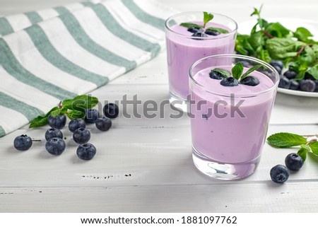 Blueberry yogurt served with fresh blueberries and mint leaves. Two glasses of yogurt on a white wooden table. Healthy breakfast.