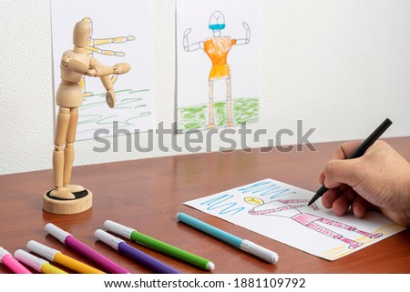 Man painting with black marker a drawing he makes from a wooden human figure and then coloring with various markers