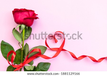 Red rose with red ribbon in shape of heart on pink background. Concept of Valentine's day, mother's day, women's day and birthday. Greetings card. Copy space and Flat lay.