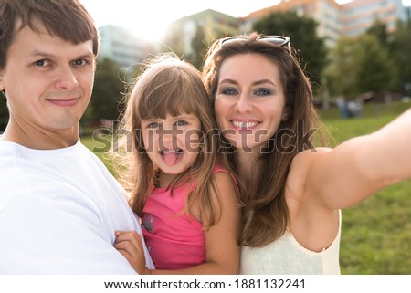 Young family man woman and child daughter 5-7 years old, summer park, selfie photo on phone, outdoor recreation posing. concept of happy family, joyfully smiling and having fun. Love in relationship