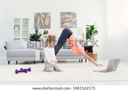Young adorable mom makes stretching exercises and practicing yoga with baby girl at home. Health care and sports concept