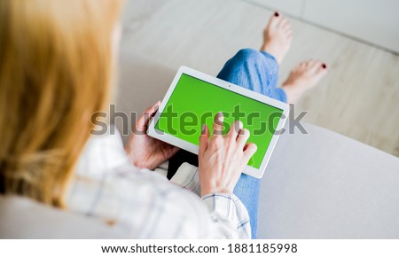 Young woman is relaxing on comfortable couch and using tablet at home