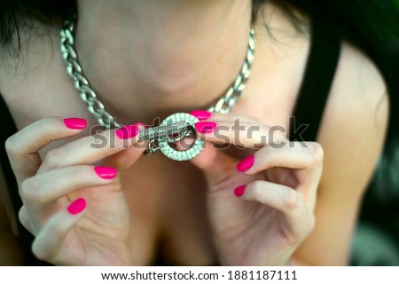 Silver metal massive chain on womans neck. close up image. Ring, phalanx ring on a female hand and luxurious chain with pendants-silver key and white gold disk