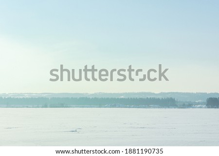 Winter landscape with field, trees and blue sky,long horizontal composition. Light fog and haze over the forest. Natural atmospheric cold background. View from the car window on the snow-covered trees
