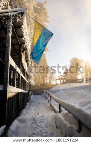 Snow-covered trail in the mountains, the flag of Ukraine in the frost on a sunny snowy day, the Carpathian roads.