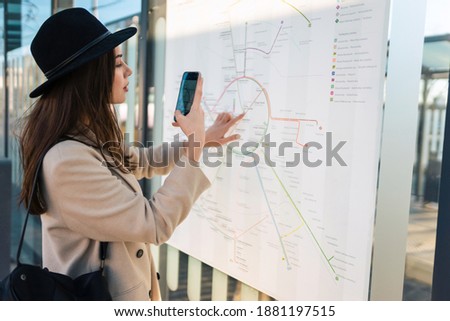 Traveler woman at bus stop takes photo of map public transport routes