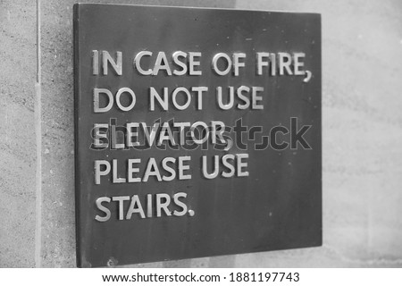 A sign that says, In Case Of Fire, Do Not Use Elevator, Please Use Stairs, which direct people of what to do in case of an fire emergency. Black and White Photo.