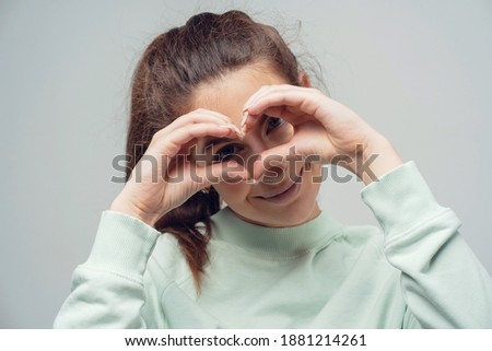 a two-handed heart gesture shows near the face, a young confident woman of Caucasian appearance. Clothing white fluffy warm stylish jacket. copy space