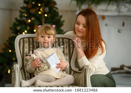 Little funny cute blond girl in a chair her lovely mother together in front of Christmas tree