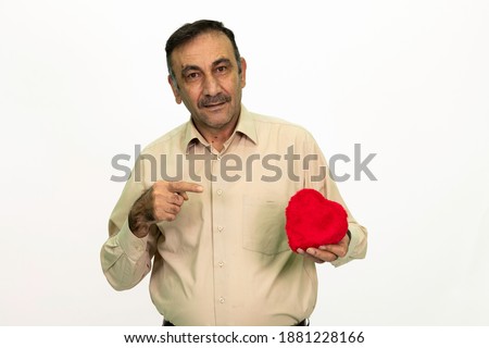 Mature man holding a heart shaped gift box in his hand. The man is dressed in a yellow shirt and cloth pants. Isolated image white background