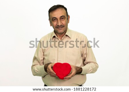 Mature man holding a heart shaped gift box in his hand. The man is dressed in a yellow shirt and cloth pants. Isolated image white background