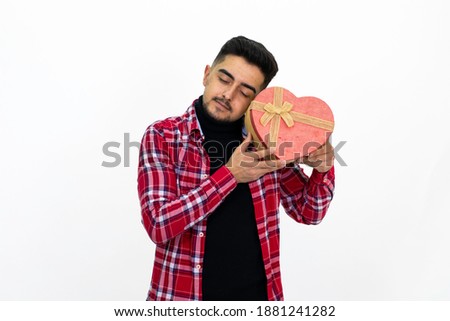 Young male holding a heart-shaped gift box in his hand. Wearing a striped shirt. White background, isolated image.