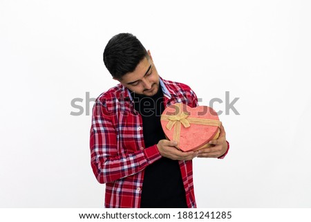 Young male holding a heart-shaped gift box in his hand. Wearing a striped shirt. White background, isolated image.