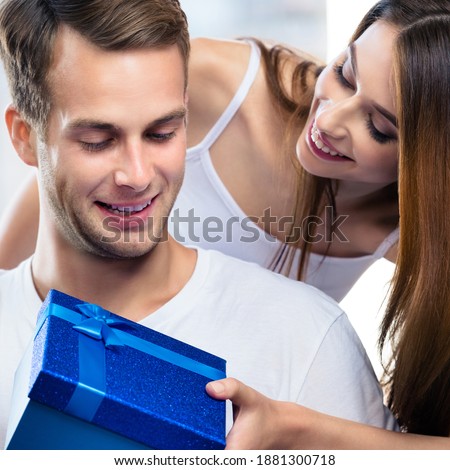 Happy amazed smiling couple with gift box, at home. Shopping, sales, holidays love, relationship concept - young man and woman together, indoors. Square composition.