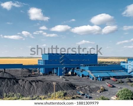 Dump of coal. A high pile, aerial view. A blue industrial building is visible in the background.