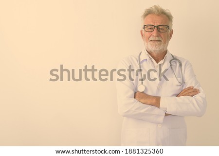 Studio shot of handsome senior bearded man doctor with arms crossed against white background