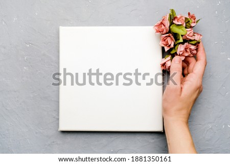 Female hand and blank canvas board with tiny flowers. Mockup poster frame. Woman day, spring concept.