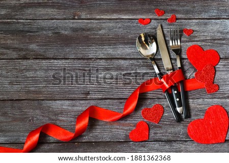 Table setting for celebration Valentine's Day. Wooden table place setting and silverware with red hearts for Valentine day. Holiday concept.