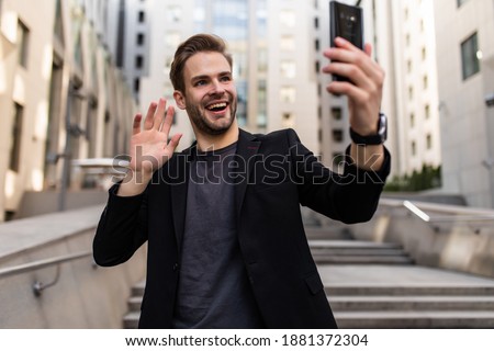 A successful handsome businessman in a suit, holding a mobile phone in his hand, making a selfie, a background of skyscrapers.