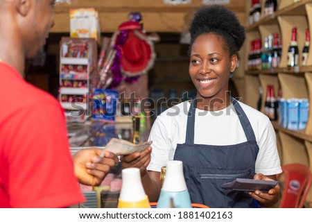 female african shop attendant smiling while collecting money from a customer Royalty-Free Stock Photo #1881402163