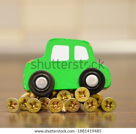 A selective focus shot of a green toy car on som golden screws on a wooden surface