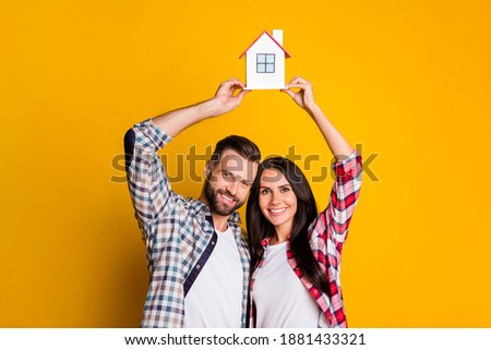 Photo portrait of small family holding house model over head isolated on vivid yellow colored background