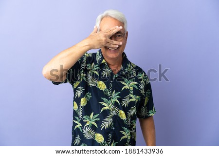 Middle age Brazilian man isolated on purple background covering eyes by hands and smiling