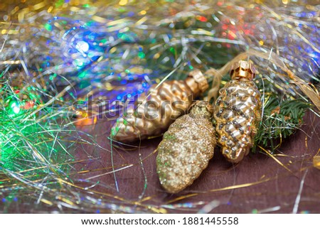 Three golden cones (ceramic Christmas decorations) on the branch of spruce with the colorful garland and tinsel. New year background 
