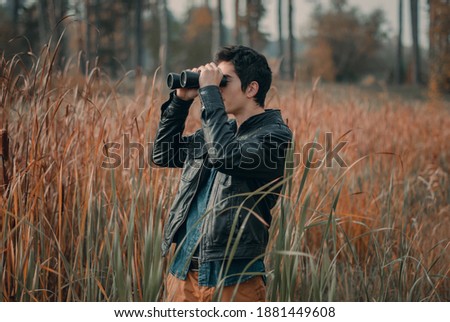 
young man with binoculars looks into the distance on the background of nature