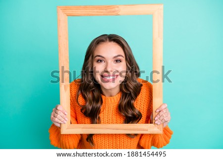 Photo of young smiling cheerful pretty attractive girl looking through wooden frame isolated on turquoise color background