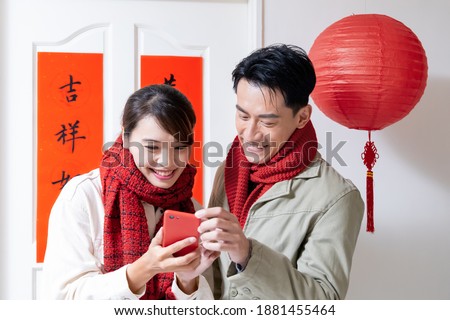 Loving asian young couple making a selfie in front of the door and looking to their photos with spring festival couplets