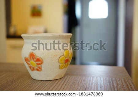a closeup sot of a decorated clay pot with flower details on a wooden table